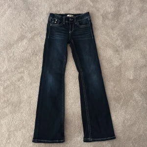 Mörkblå bootcut jeans från Gina Tricot - Snygga mörkblå bootcut jeans från Gina Tricot med kontrastsömmar och knappar på bakfickorna. Perfekta för en avslappnad stil med en touch av retro. Passar bra till både sneakers och boots.