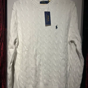 Vit stickad tröja från Polo Ralph Lauren - Säljer en stilren vit stickad tröja från Polo Ralph Lauren med klassiskt kabelstickat mönster. Tröjan har långa ärmar och en rund halsringning. Perfekt för en elegant och avslappnad look. OBS! Priset är inte hugget i sten. Hör av er vid minsta fundering 🍾
