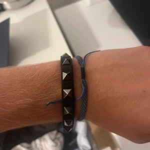 Svart valentino  armband - Snyggt svart valentino armband med silverfärgade pyramidnitar. Perfekt för att ge en grisch stil. Bra till sommaren!Armbandet har en justerbar rem för att passa olika storlekar. KÖPT PÅ VINTED INGET OG MEDFÖLJANDE! Namn ROCKSTUD LEATHER BRACELET Nypris SEK 3.085,00 sista biten av lädret har gått upp och sen limmat ihop men syns ingenting när man har det på sig. Skick avgör själv se sista bilden. Visa nitar är lite repiga men syns knappt.Vid frågor tveka inte av att höra av er! 