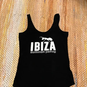 Svart linnetopp med Ibiza-tryck - Snygg svart linnetopp med vitt Ibiza summer party-tryck framtill. Perfekt för sommarens alla fester och strandhäng. Toppen har en enkel och stilren design med breda axelband.