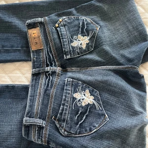 Snygga bootcut jeans med brodering - Hej! Jag säljer dessa jeansen då det var för små för mig, jeansen är bootcut och med en fin brodering på bakfickorna. De är från H.T.T jeans. Midjemått är 34-35 och innerbenslängden är 84 cm. Pristet är som de är då jag själv köpte dem för runt den summan.  