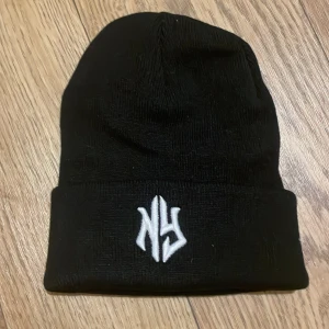 Svart mössa med broderad logga - Snygg svart mössa med vit broderad 'NY'-logga framtill. Perfekt för att hålla värmen under kyliga dagar. Enkel och stilren design som passar till det mesta.