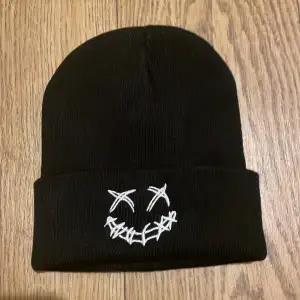 Snygg svart stickad mössa med en unik broderad design framtill. Perfekt för att hålla värmen och samtidigt se cool ut. Passar bra till både vardag och speciella tillfällen.