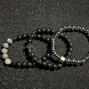 3 Pack pärlarmband - Tre stilrena armband med svarta och grå pärlor. Ett av armbanden har en korsdetalj och vita marmorerade pärlor. Perfekt för att ge en edgy touch till din stil.