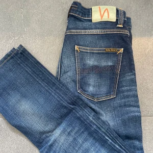 Nudie Jeans - Säljer ett par klassiska mörkblå jeans från Nudie Jeans med snygga slitningar och kontrastsömmar. Modellen har fem fickor, orange detaljer och normal passform.                                    Storlek: 30/32.                                                                  Skick: Mycket bra😊