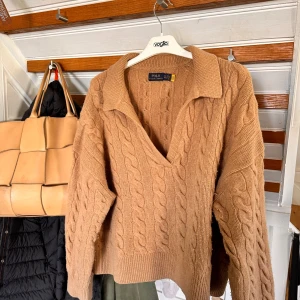Beige kabelstickad tröja från Polo Ralph Lauren - Säljer en beige kabelstickad tröja från Polo Ralph Lauren. Tröjan har krage, v-ringning och långa ärmar. Den är gjord i ett mjukt stickat material och har en klassisk, tidlös look. 90% Ull 10% Cashmere