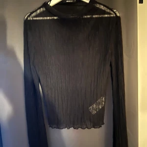 Svart tröja från Gina Tricot - Säljer en svart långärmad tröja från Gina Tricot. Tröjan är transparent och har en ribbad struktur med lätt vågig nederkant. Perfekt att styla lager på lager för en trendig look.
