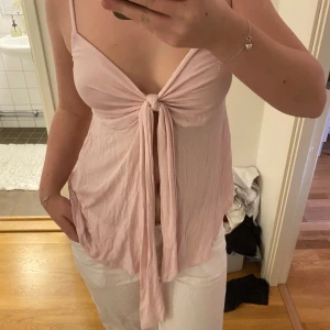 Ljusrosa linnetopp med knyt framtill - Säljer en ljusrosa linnetopp från Gina Tricot med smala axelband och snygg knytning framtill. Toppen är ärmlös och har en avslappnad passform, perfekt för varma dagar.