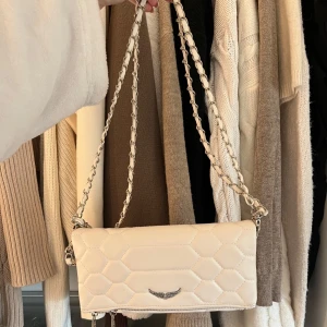 Vit quiltad axelväska med kedja - Snygg vit axelväska med quiltat mönster och silverfärgad kedja. Väskan har en dragkedja på baksidan för extra förvaring. Perfekt för att ge din outfit en stilren touch.