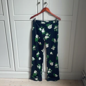 Blommiga byxor från Twist & Tango - Mörkblå byxor med vitt och grönt blommönster från Twist & Tango. Byxorna har raka ben och normal passform, perfekta för dig som gillar färg och mönster. Byxorna har varit väl omhändertagna men har några små tråddragningar längst ner. 