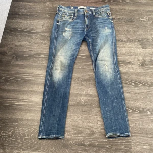 Blå Replay Anbass jeans - Säljer ett par blå Replay Anbass jeans med slitningar och ljusa partier framtill. Klassisk femficksmodell med dragkedja och knapp.  Perfekta till alla tillfällen