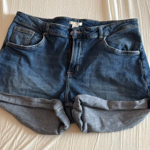 Blå jeansshorts med upprullad kant - Klassiska blå jeansshorts från H&M med upprullad kant och femficksmodell. Perfekta för varma dagar och har en normal passform med knapp- och dragkedjestängning. Tidlös design som passar till det mesta.