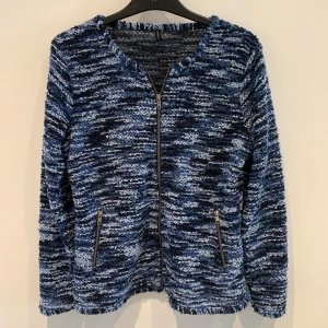 Blåmelerad stickad jacka med dragkedja - Säljer en blåmelerad stickad jacka med dragkedja framtill och två snedställda fickor med dragkedja. Jackan har lång ärm och är i ett mjukt, texturerat material. Perfekt för dig som gillar en avslappnad men ändå snygg stil.