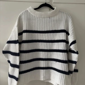 Vit och marinblå randig stickad tröja - Säljer en vit stickad tröja med marinblå horisontella ränder. Tröjan har en bred ribbad krage och långa ärmar. Den är oversized och har en mysig, avslappnad passform. Perfekt för kyliga dagar.
