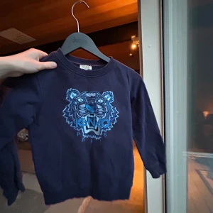 Mörkblå sweatshirt med tiger från Kenzo Kids - Cool mörkblå sweatshirt från Kenzo Kids med broderad tiger i blå toner på bröstet. Tröjan har rund hals och långa ärmar. Perfekt för dig som gillar statement-plagg och snygga detaljer.