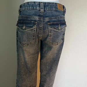 Blå bootcut jeans med fickdetaljer - blå bootcut jeans med snygga slitningar och markerade sömmar. 