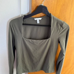 Olivgrön långärmad topp med fyrkantig ringning från H&M - Snygg olivgrön långärmad topp från H&M med trendig fyrkantig ringning. Modellen är croppad och har en tight passform, perfekt att styla till jeans eller kjol.