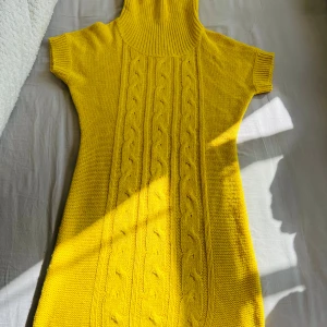 Gul stickad poloklänning - Säljer en gul stickad klänning med polokrage och korta ärmar. Klänningen har ett fint kabelstickat mönster framtill och är i en mjuk, varm kvalitet. Perfekt för dig som vill ha något färgglatt och mysigt.