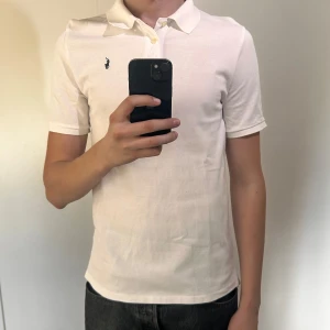 Vit pikétröja från Ralph Lauren - Obs ( storlek Xl för barn så mellan S-M för vuxen) Klassisk vit pikétröja från Ralph Lauren med korta ärmar och liten broderad logga på bröstet. Tröjan har krage och knappar framtill, perfekt för en clean och stilren look. 