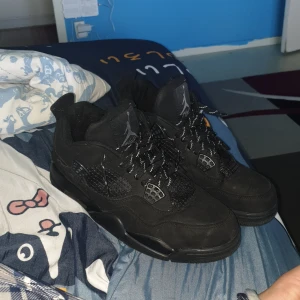 Svarta Nike Air Jordans - Säljer ett par helsvarta Nike Air Jordans med klassisk siluett och Jumpman-logga på både plös och häl. Skorna har snörning och mönstrade svarta skosnören samt rund tå och platt sula. Perfekta för dig som gillar streetwear och vill ha en stilren look.