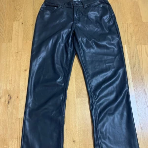 Svarta skinnbyxor från 157 - Snygga svarta skinnbyxor från 157 med klassisk femficksdesign och raka ben. Byxorna har normal passform och stängs med knapp och dragkedja. Perfekta för dig som vill ha en cool och stilren look.