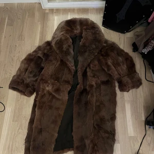 Brun pälsjacka med bred krage - Säljer en lång, brun pälsjacka med bred krage och generösa ärmar. Jackan har en klassisk och lyxig look, perfekt för att hålla värmen under kallare dagar. Fodrad insida för extra komfort. *äkta päls*