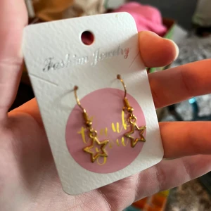 Guldiga örhängen med stjärnhänge - Säljer ett par snygga guldiga örhängen med hängande stjärnor. Egebgjorda. Perfekta för att ge din look lite extra glans och stil. Passar dig som gillar unika detaljer och trendiga accessoarer.