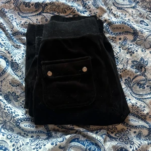 Svarta velourbyxor från Juicy Couture - Säljer ett par svarta velourbyxor från Juicy Couture i storlek XS. Byxorna har en ficka med knappar bak och snörning i midjan. Perfekta för en avslappnad och trendig look.