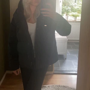 Svart pufferjacka - Säljer en svart pufferjacka med dragkedja och knappar. Jackan har lång ärm och hög krage, perfekt för kyligare dagar. Enkel och stilren design som passar till det mesta.