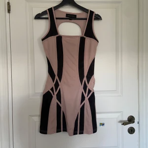 Beige och svart kortklänning från House of Deréon - Säljer en snygg beige/rosa och svart kortklänning från House of Deréon. Klänningen har breda axelband, cut-out detalj i ryggen och grafiska svarta paneler framtill som ger en cool look. Perfekt för dig som vill sticka ut.
