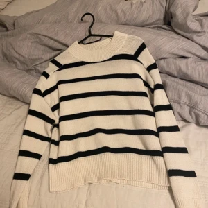 Vit och svart randig stickad tröja från Amisu - Säljer en stickad tröja från Amisu i storlek S. Tröjan är vit med svarta horisontella ränder, har lång ärm och bred ribbad kant vid hals, ärmslut och nederkant. Perfekt för en stilren och avslappnad look.