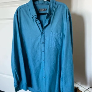 Blå skjorta från Dressmann - Säljer en blå långärmad skjorta från Dressmann i slim fit-modell. Skjortan har klassisk krage, knäppning framtill och en bröstficka. Perfekt för dig som gillar enkel och stilren design.