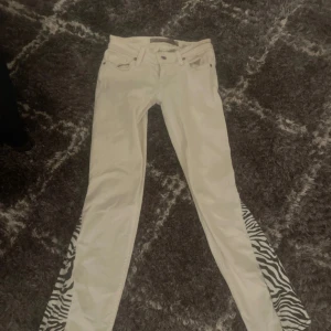 Vita jeansbyxor från Guess med zebramönster - Säljer ett par ascoola vita jeans från Guess med zebramönstrade detaljer längs sidorna. Byxorna har normal passform. Perfekta för dig som vill sticka ut med en unik detalj på dina jeans.💘💘