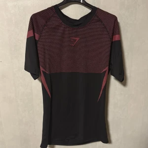 Svart och röd Gymshark träningstshirt - Säljer en svart och röd kortärmad träningstshirt från Gymshark. Väldigt sällsynt och väldigt snygg. Säljer också denna efter jag använt den ett par gånger och blivit trött på den.