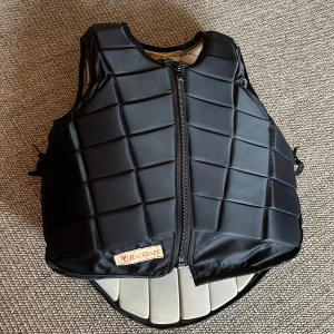  Racesafe väst - Säljer denna svarta ridväst från Racesafe. Den är i ett gott skick utan några defekter. Den är i storlek L junior vilket jag skulle säga motsvarar XS i damstorlek och den är BETA Certification Markt!