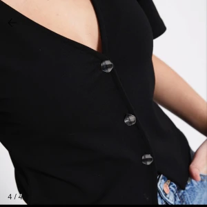 Svart kortärmad topp från 157 - Svart kortärmad topp från 157 med v-ringning och tre knappar framtill. Modellen är croppad och har en enkel, stilren look som passar till jeans eller kjol. Tillverkad i mjukt bomullsmaterial för en skön känsla.