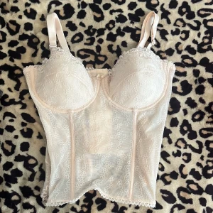 Beige spetskorsett med blommönster - Supersöt beige korsett med broderade blommor och spetsdetaljer. Justerbara axelband och hakknäppning bak. Transparent mesh och vackra volangkanter nertill ger en romantisk vibe. Perfekt att styla med jeans eller kjol för en trendig look.