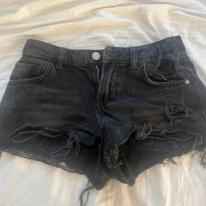 Lågmidjade Svarta jeansshorts från Zara - Snygga svarta jeansshorts från Zara med råa, fransiga kanter och slitna detaljer framtill. Är i storlek 32 men skulle säga att dem passsr 34 bättre💕