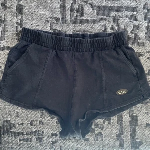 Svarta shorts  - Svarta shorts med elastisk midja och fickor både fram och bak. Mjukt bomullsmaterial och en liten logga på ena sidan. Perfekta för chill dagar eller när du vill ha något bekvämt och enkelt.