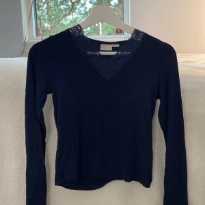 Mörkblå topp med spets från Gina Tricot - Supersnygg mörkblå långärmad topp från Gina Tricot med v-ringning och spetsdetaljer runt halsen. Toppens material känns mjukt och stretchigt, perfekt till jeans eller kjol. Enkel men ändå med en extra touch tack vare spetsen.