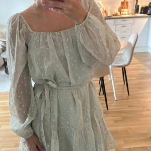  Grön klänning med volang - Superfin ljus kort klänning med transparenta långärmar, volangkant och knytband i midjan. Prickigt mönster (silver glittriga) och fyrkantig ringning. Storlek 34 men är mer som 36