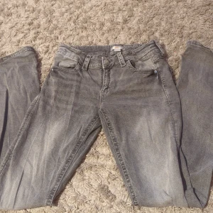 Grå jeans med detaljerade bakfickor - Snygga grå jeans med slitningseffekt och coola detaljerade bakfickor med knappar. Klassisk femficksmodell och bälteshällor. Perfekta för dig som gillar en avslappnad men ändå trendig look.