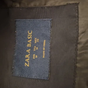 Marinblå pufferjacka från Zara Basic - Snygg svart pufferjacka från Zara Basic i storlek M. Jackan har hög krage, dragkedja och knappar framtill samt praktiska fickor med dragkedja. Perfekt för kyliga dagar och ger en clean och modern look.