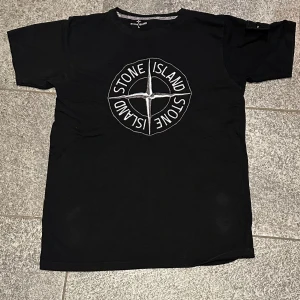 Stone Island t-shirt  - Svart t-shirt från Stone Island i bomull med stor broderad logga på bröstet och klassisk patch på ärmen. T-shirten har rund hals och korta ärmar, perfekt för en clean och stilren streetwear-look.