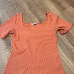 Ribbad orange topp från Pieces - Snygg ribbad topp i orange från Pieces med fyrkantig ringning och korta ärmar. Storlek L