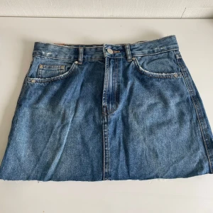 Low waised jeanskjol - Snygg blå jeanskjol med klassiska fickor fram och bak, samt rå, avklippt kant nertill för en cool vibe. Kjolen har knapp och dragkedja framtill och är perfekt för dig som gillar en avslappnad stil. Low waised skriv för bilder❤️