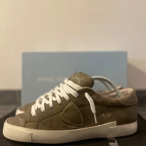 Olivgröna sneakers från Philippe Model - Säljer dessa fina olivgröna sneakers från Philippe Model med vit sula och vita snören. Skorna är i skinn och har en klassisk låg profil med rund tå och diskret logodetalj på sidan. Bra skick! Riktigt fina skor. Storlek 41. Allt org medföljer! Priset är diskuterbart. Nypris runt 3500 kr!