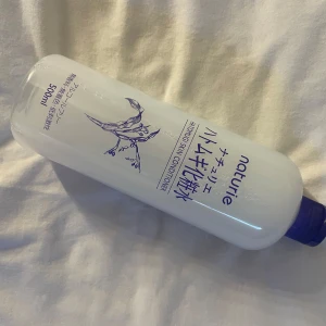 Naturie Hatomugi Skin Conditioner - Stor flaska (500 ml) av Naturie Hatomugi Skin Conditioner, en populär japansk toner. Kommer i genomskinlig plastflaska med lila lock och blå text. Perfekt för att återfukta huden och förbereda inför smink. Innehåller extrakt av korn (hatomugi).