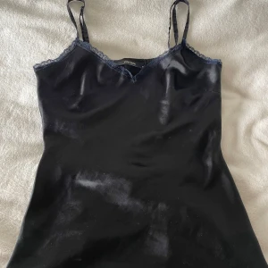 Svart satinlinne från Vero Moda - Snyggt svart linne från Vero Moda i satinliknande material med tunna axelband och spetsdetaljer vid v-ringningen. Storlek S. Pris kan diskuteras💕