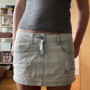 Ljusgrå jeanskjol med slitningar - Snygg ljusgrå jeanskjol med slitna detaljer och råa kanter. Kjolen har klassiska fem fickor, bälteshällor och dragkedja framtill. Perfekt för dig som gillar en avslappnad och trendig stil. 🩶 passar perfekt på mig som brukar ha 36/38 och vill att kjolen ska sitta på höfterna. 